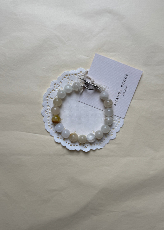 Eggshell beaded bracelet by AMANDA BUGGE studio – handmade jewelry in beige and white tones with silver toggle clasp, displayed on lace-edged cotton cloth