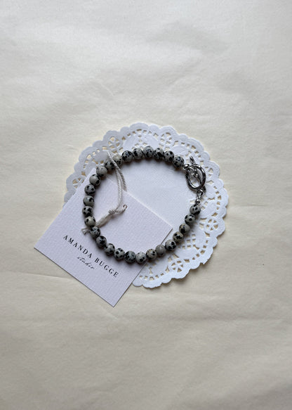 Petite Dalmatian beaded bracelet by AMANDA BUGGE studio – handmade jewelry in black and white tones with silver toggle clasp, displayed on lace-edged cotton cloth