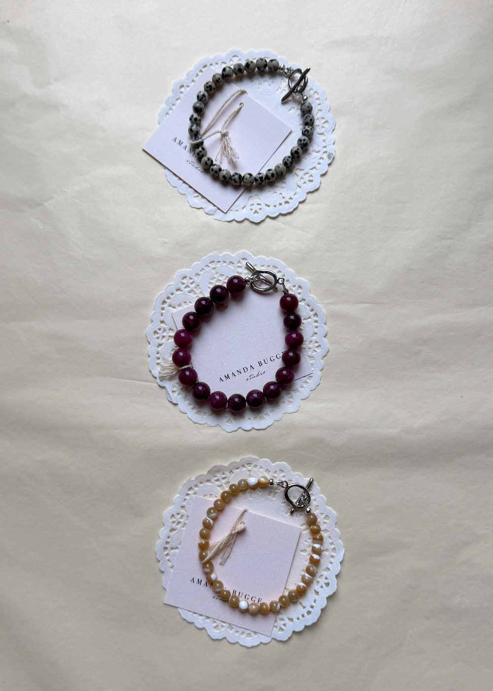 Petite Dalmatian, plum and petite toffee beaded bracelet by AMANDA BUGGE studio – handmade jewelry in dalmatian, plum and beige tones with silver toggle clasp, displayed on lace-edged cotton cloth