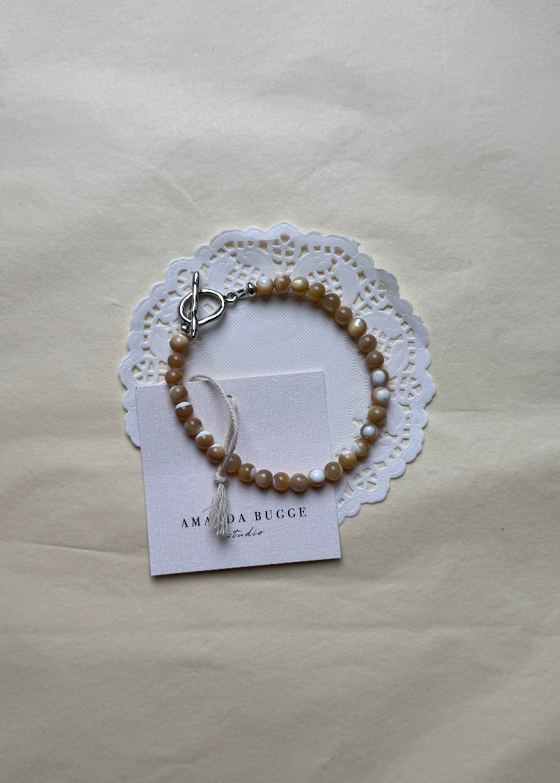 Petite Toffee beaded bracelet by AMANDA BUGGE studio – handmade jewelry in beige tones with silver toggle clasp, displayed on lace-edged cotton cloth