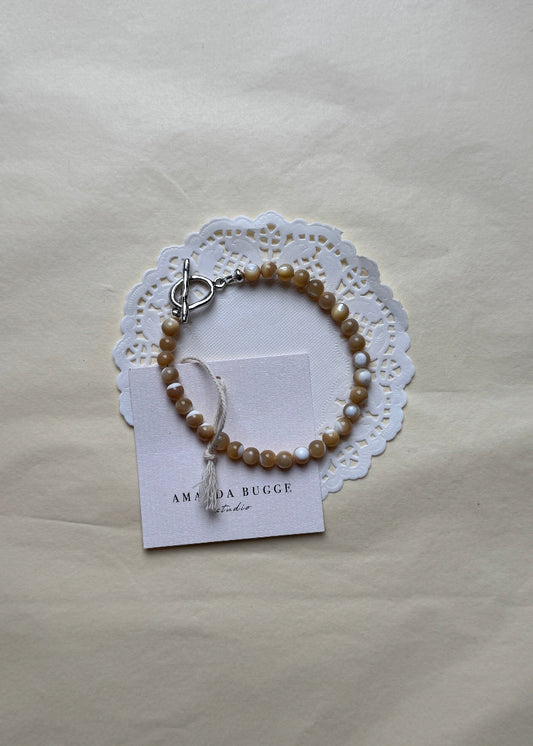 Petite Toffee beaded bracelet by AMANDA BUGGE studio – handmade jewelry in beige tones with silver toggle clasp, displayed on lace-edged cotton cloth