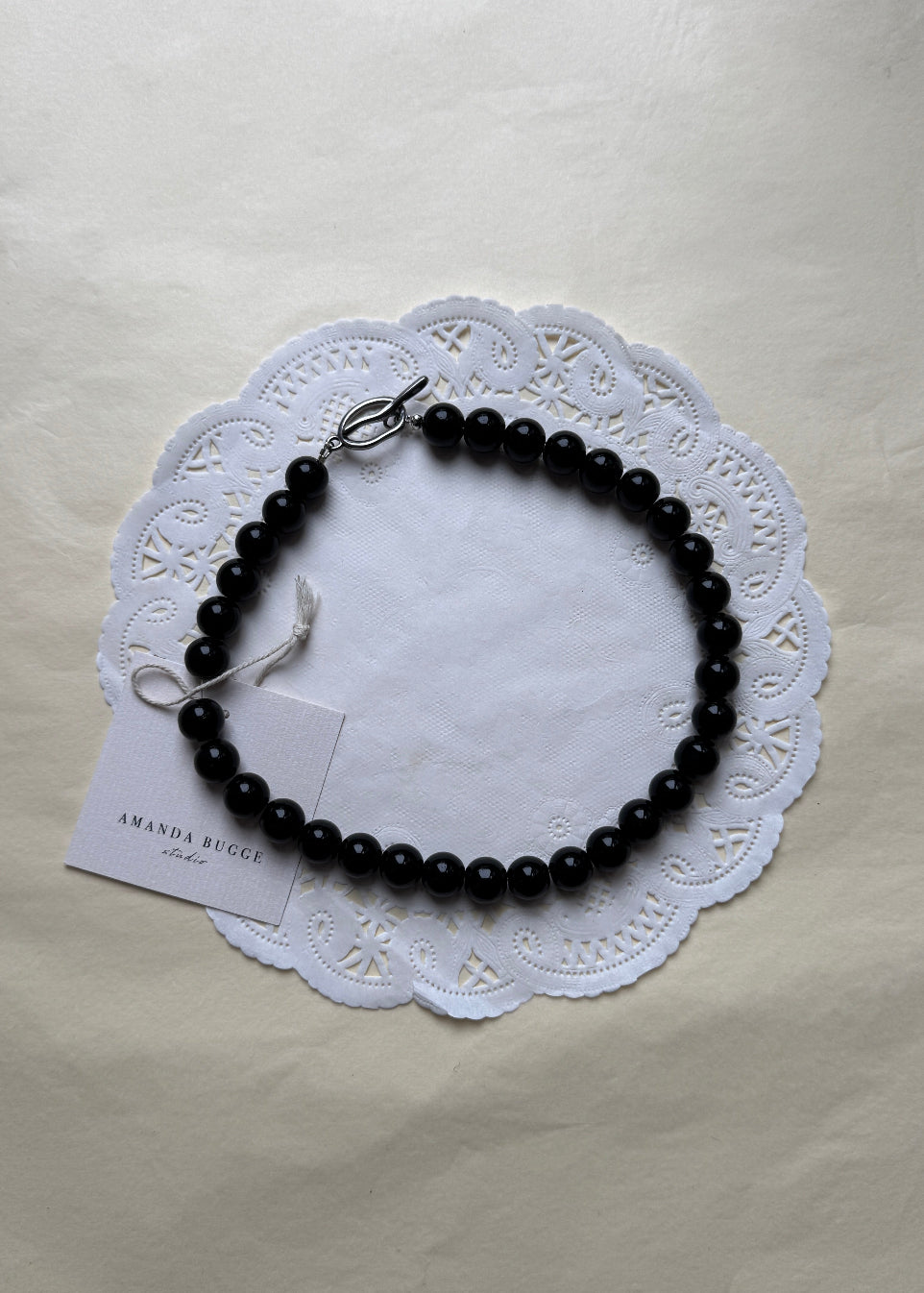 Bold Dalmatian necklace by AMANDA BUGGE studio – minimalist jet black beaded choker necklace with silver toggle clasp, styled on white lace-edged fabric

