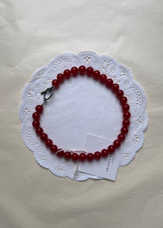 Bold Dalmatian necklace by AMANDA BUGGE studio – minimalist red current beaded choker necklace with silver toggle clasp, styled on white lace-edged fabric
