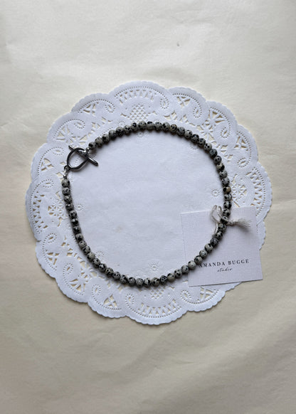 Petite Toffee beaded necklace by AMANDA BUGGE studio – handmade jewelry in dalmatian pattern with silver toggle clasp, displayed on lace-edged cotton cloth