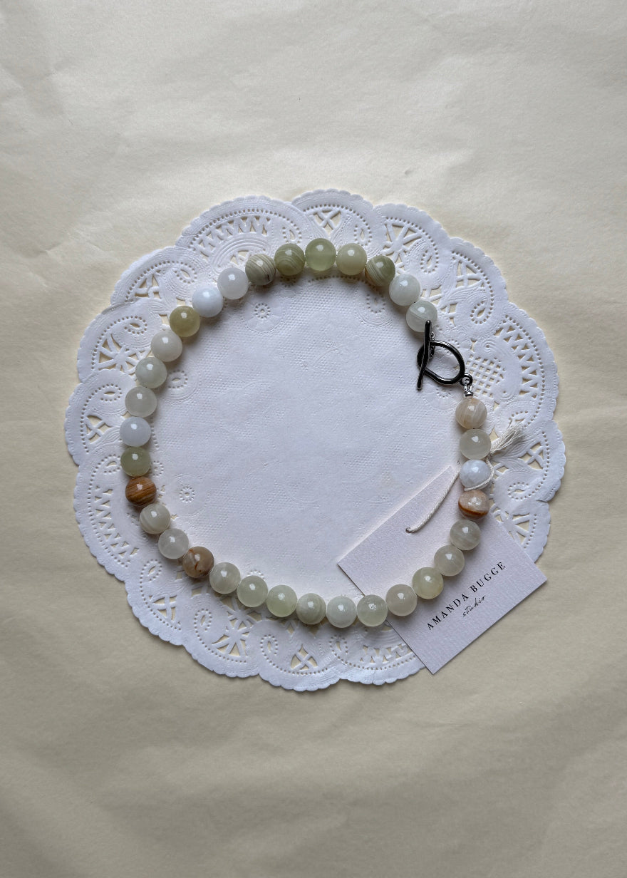 Bold Eggshell necklace by AMANDA BUGGE studio – minimalist damatian beaded choker necklace with silver toggle clasp, styled on white lace-edged fabric
