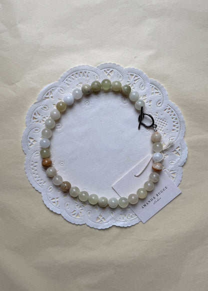 Bold Eggshell necklace by AMANDA BUGGE studio – minimalist damatian beaded choker necklace with silver toggle clasp, styled on white lace-edged fabric
