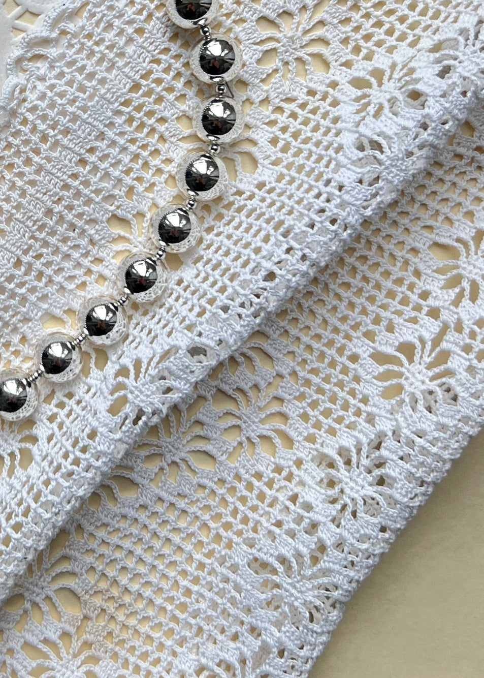 Bold silver necklace by AMANDA BUGGE studio – minimalist silver beaded choker necklace with silver toggle clasp, styled on white lace-edged lace fabric