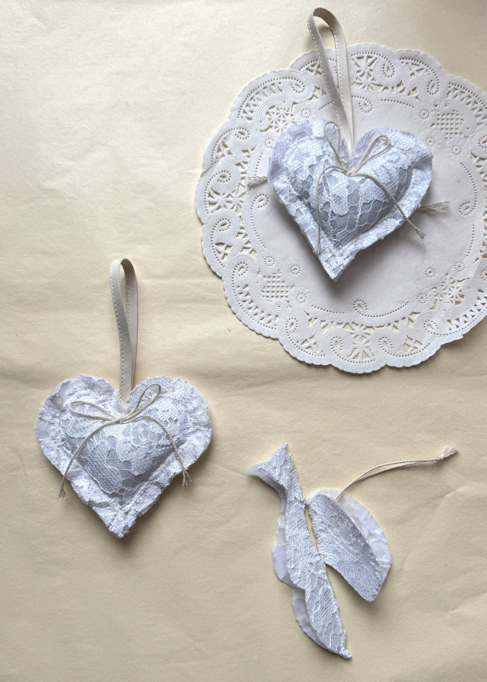 White lace Christmas heart in textile by AMANDA BUGGE studio with a ivory bow on and bird in white lace
