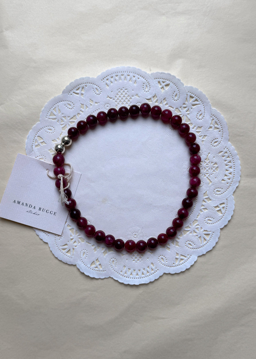 Plum beaded necklace by AMANDA BUGGE studio – handmade jewelry in plum tones with silver toggle pleated pearls, displayed on lace-edged cotton cloth