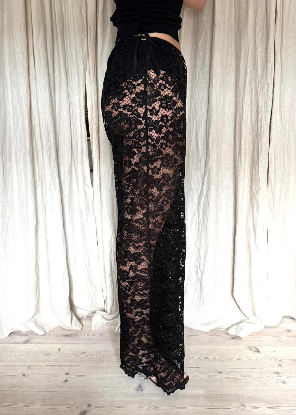 Model wearing black Nora Lace Pants in sheer lace with a relaxed fit and drawstring waist from side